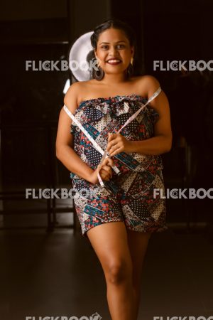 
									Fashion Design, A girl with red lipstick , tan girl , chubby girl , staring , posing , upward eyebrows ,  facial expressions , fashionable outfit , holding a measurement tape , smiling , standing 