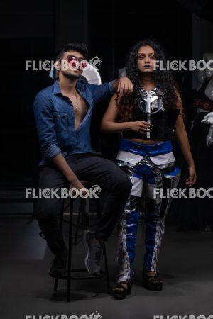 
									Fashion Design, a couple pic , A girl with blue lipstick , dark girl , curly hair , staring , posing , upward eyebrows , straight nose , facial expressions , dark skin , confident , standing , fashionable outfit , wearing a jean jacket , casual outfit , wearing sunglass , smiling , guy siting on a chair , thinking , wondering 