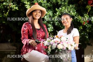
									Entertainment, Two girls with a flower bicycle , at a garden , wearing a hat , casual outfit , smiling , happy 