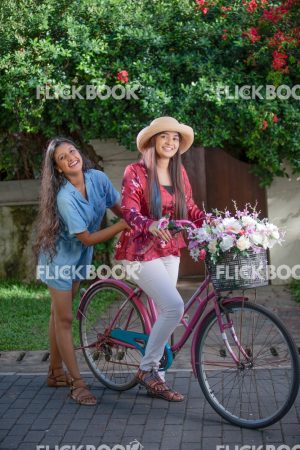 
									Entertainment, two girls with a flower bicycle , at a garden , wearing a hat , casual outfit , smiling , happy , laughing  , 