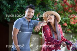 Entertainment, A couple with a flower bicycle , at a garden , wearing a hat , casual outfit , smiling , happy , , guy hand on girls shoulder , rose in mouth , girl looking at guy 