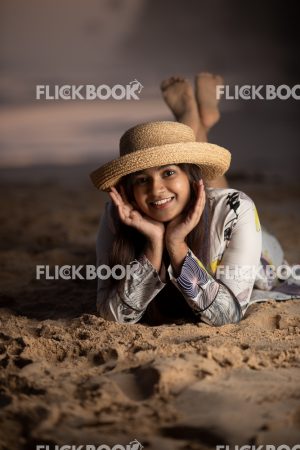 Entertainment , A girl , at beach , wearing a hat, lying down on a beach , smiling , crossed legs , smiling , happy 