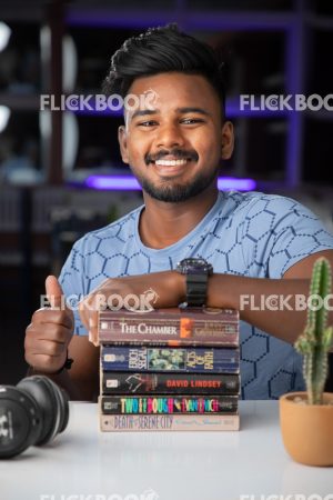 Library , books , casual outfit , sitting , happy , boy , thumbs up , smiling 
